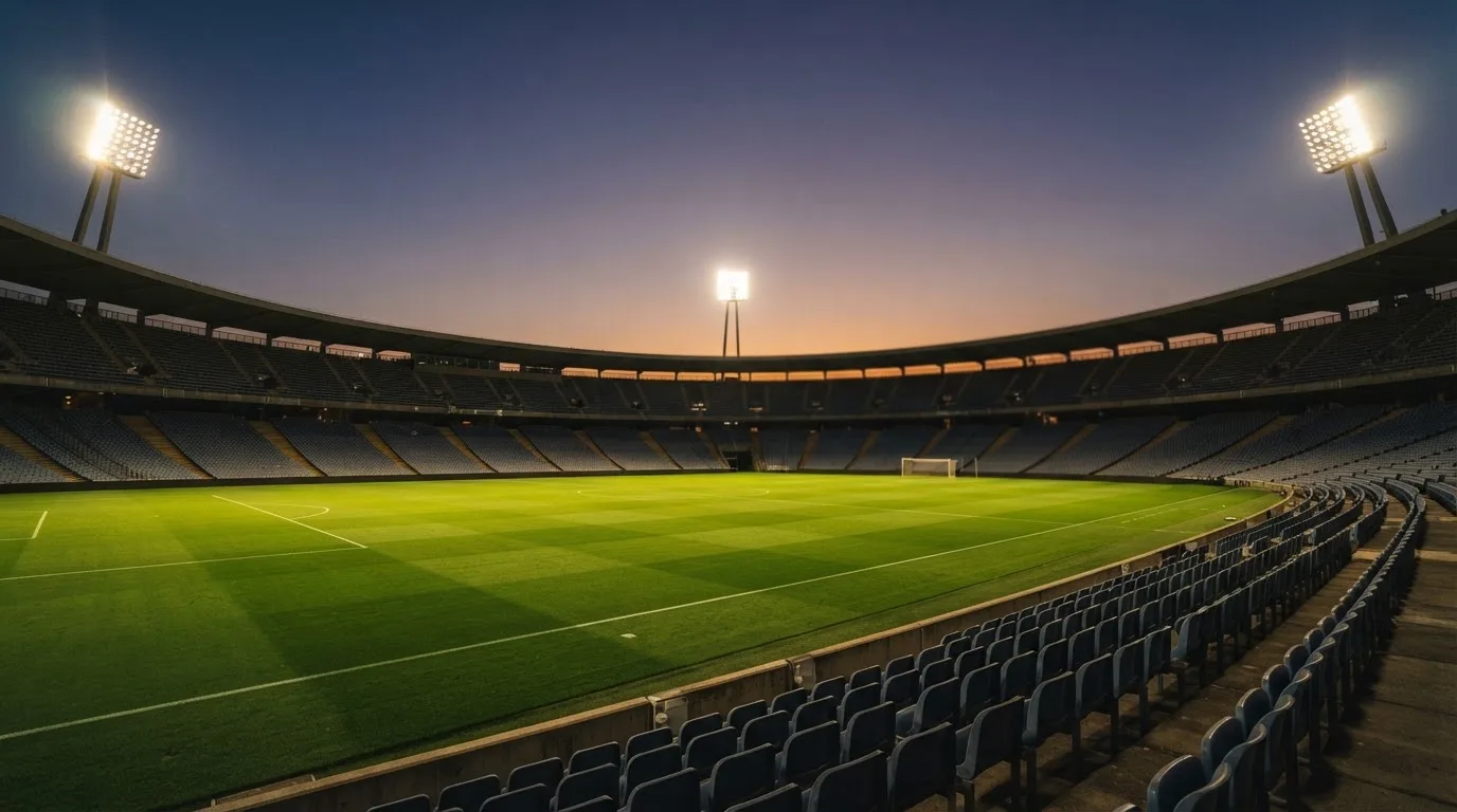 An empty football stadium with floodlight masts at dusk